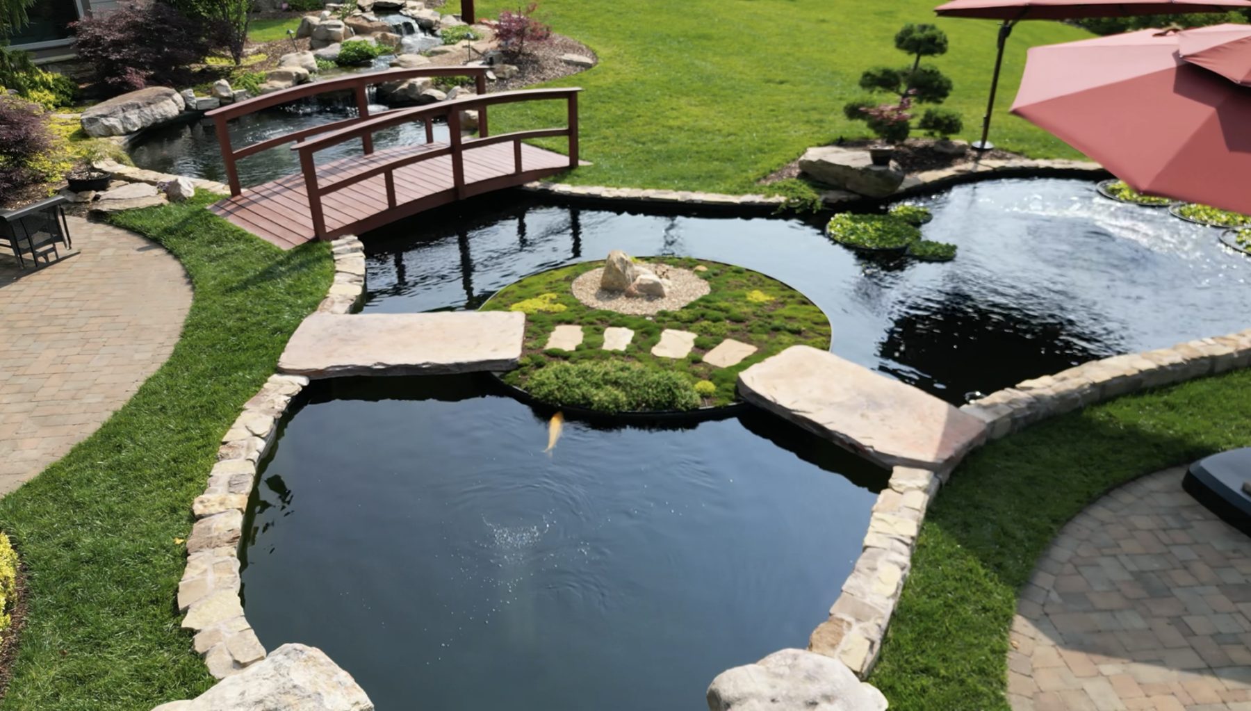 Custom concrete koi pond with natural stone edging, wooden bridge and planted island